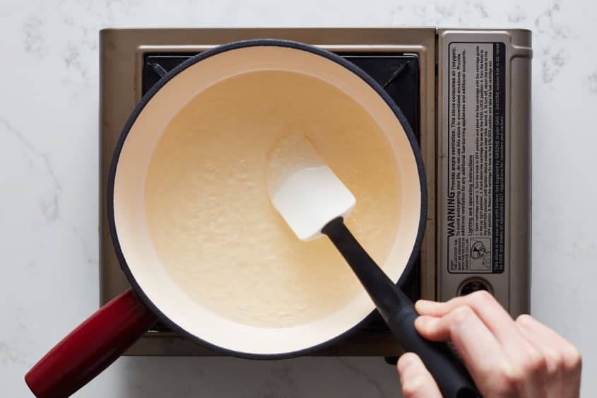 someone is mixing cheese fondue in a fondue pot with a rubber spatula
