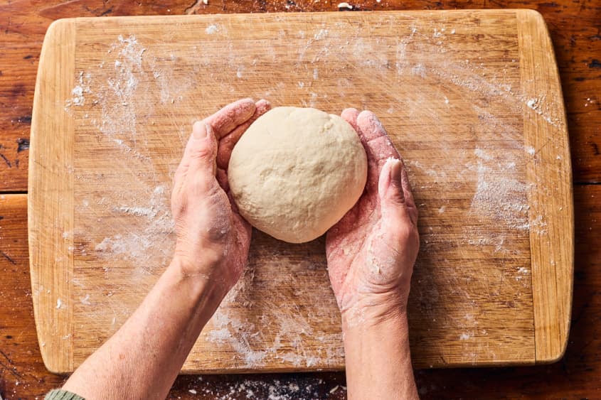 someone is kneading dough on a cutting board into a ball