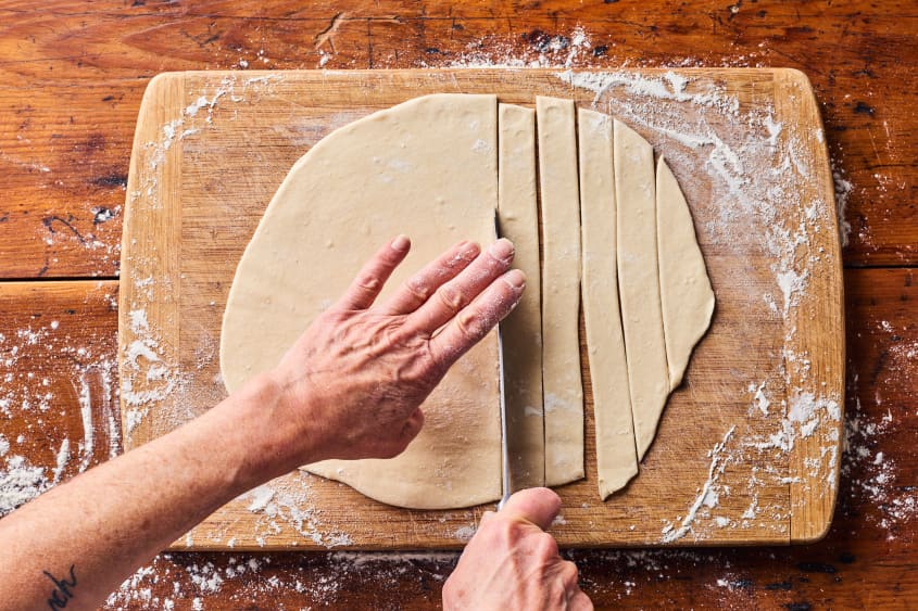 someone is cutting the flattened dough into strips