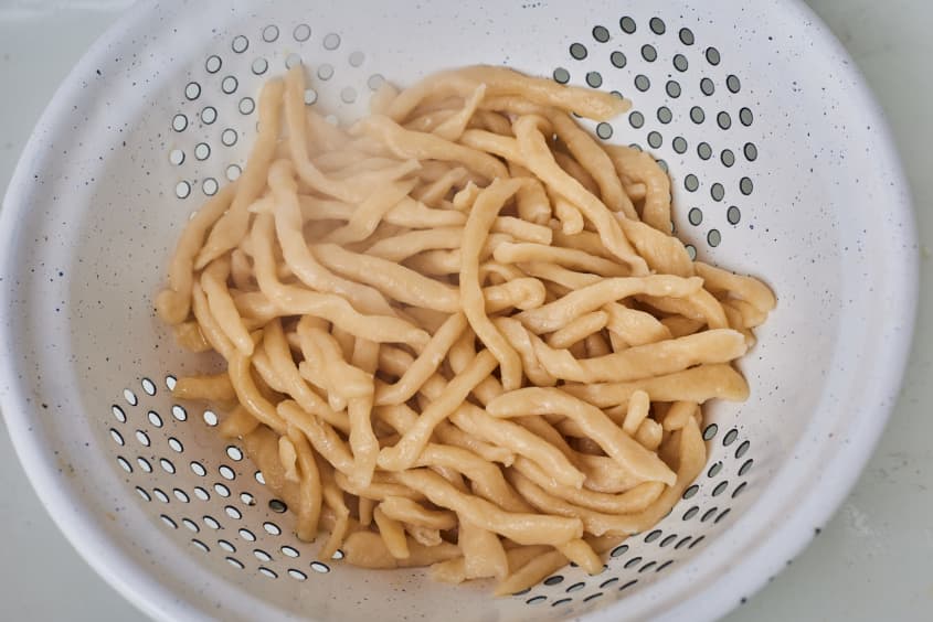 cooked strozzapreti is being rinsed in a colander