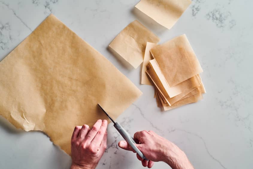 someone is cutting parchment paper into squares