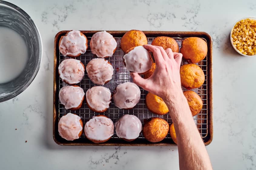 someone is placing a frosted paczki on a cooling rack