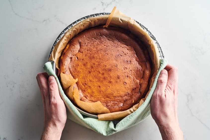 someone is holding basque cheesecake in a glass bowl out of the oven