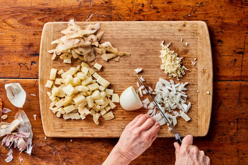 someone is chopping onions on a cutting board next to potatoes, garlic, and onion