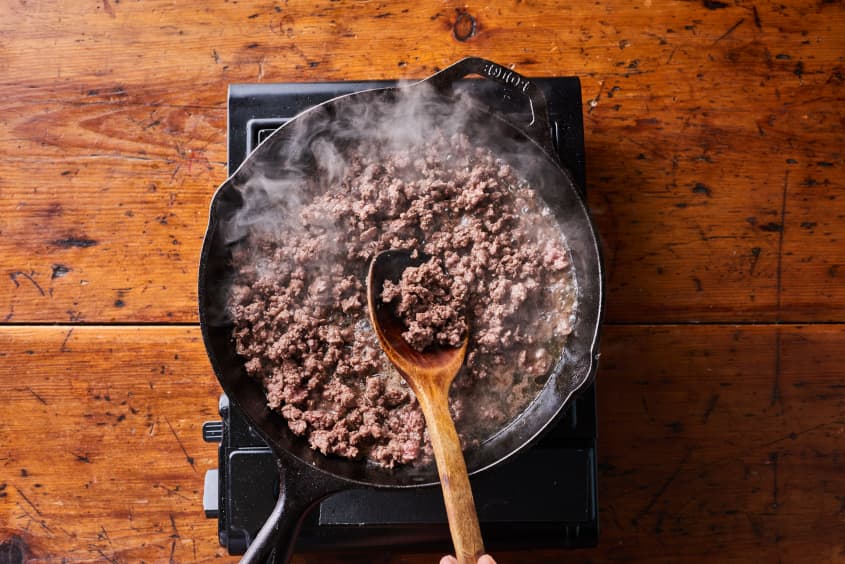 someone is stiring ground beef in a cast iron pot