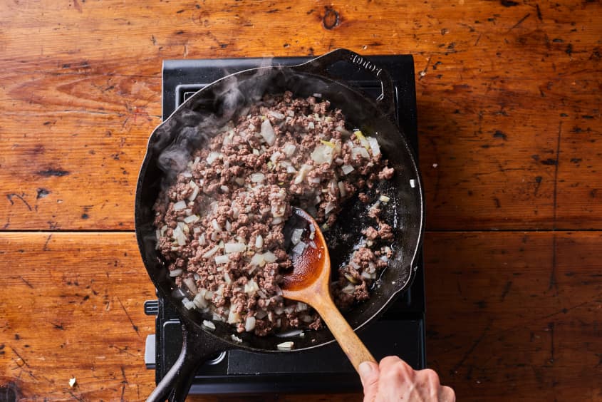 someone is stirring ground beef and onions in a cast iron pot