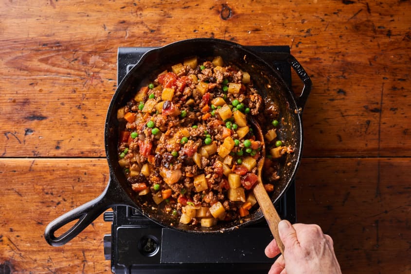 someone is stirring picadillo in a cast iron pot with a wooden spoon