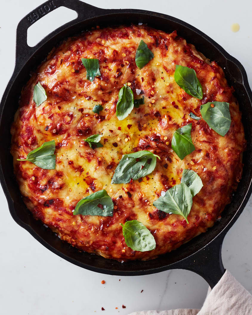 the finished pan pizza sits in a cast iron pot garnished with basil