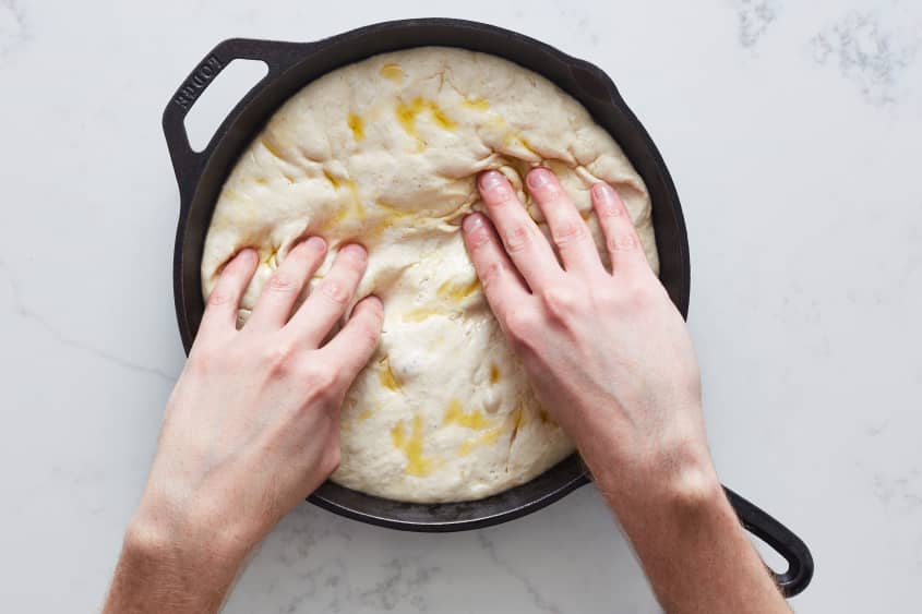 someone is pressing the dough into a cast iron pan