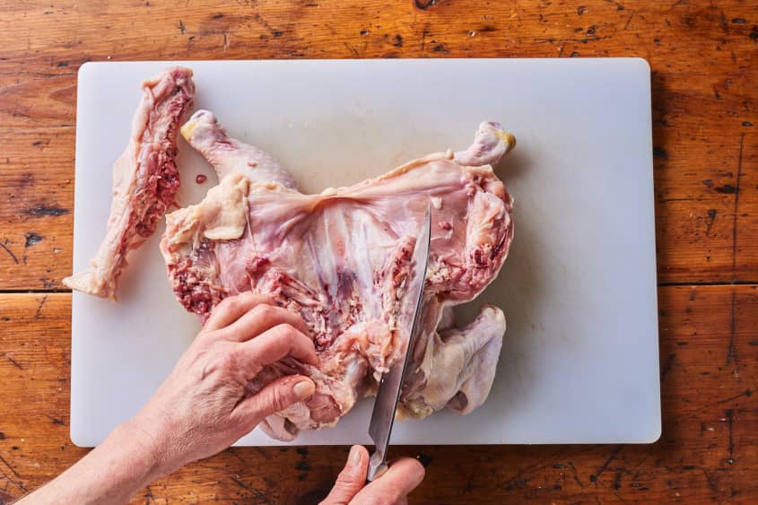 someone is removing bones by the neck of the raw chicken