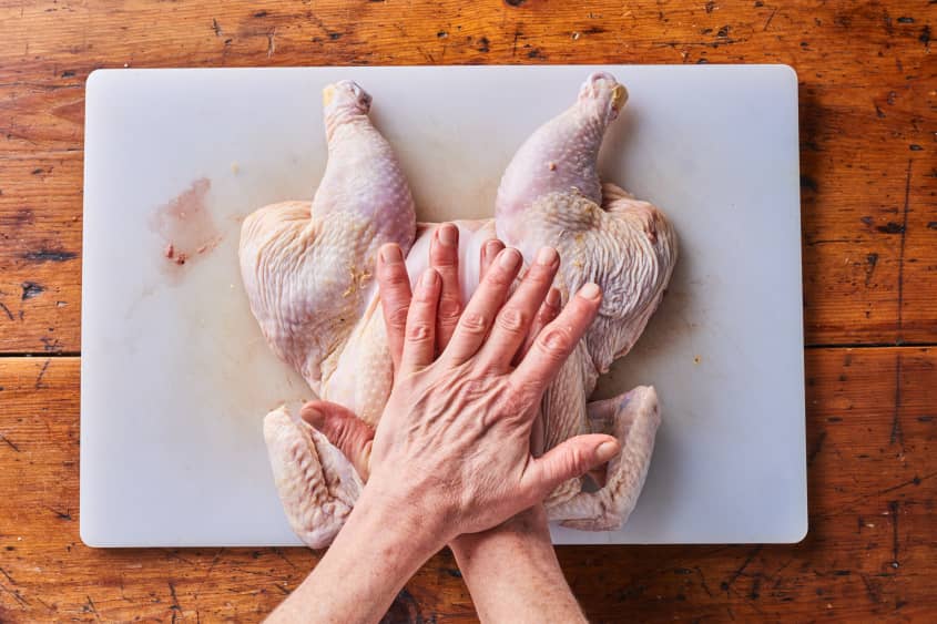 someone is pushing down a halved chicken on a cutting board