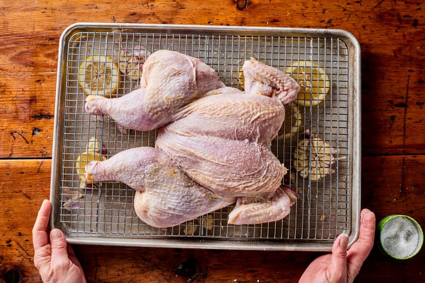 chicken sits uncooked over lemons on a metal grate