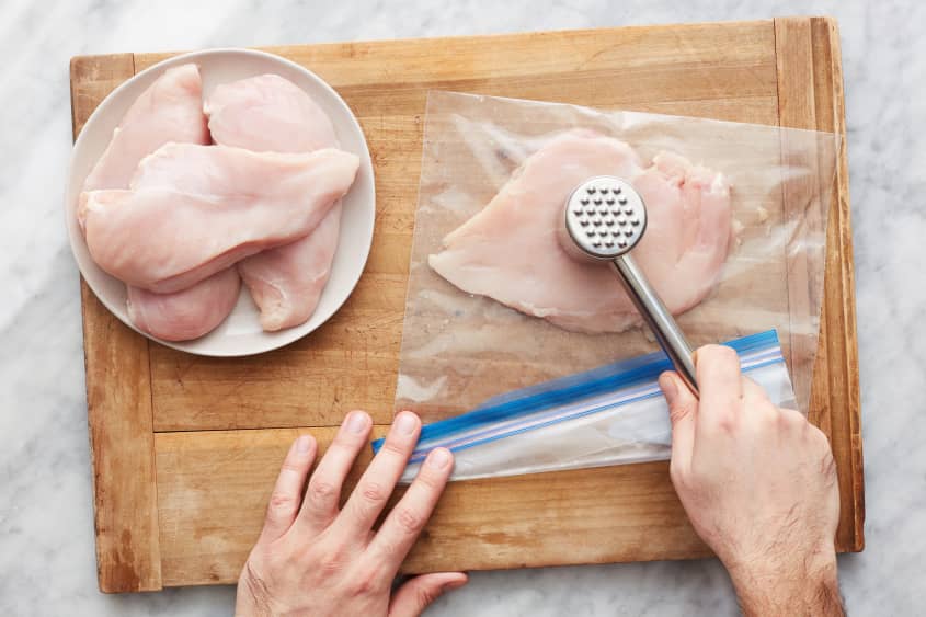 someone is pounding chicken in a plastic bag with a mallet on a cutting board