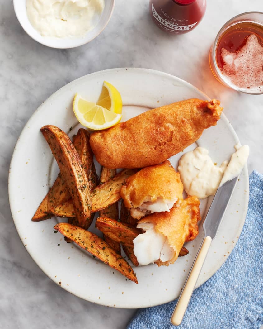 beer battered fish sits with french fried and lemons on a plate