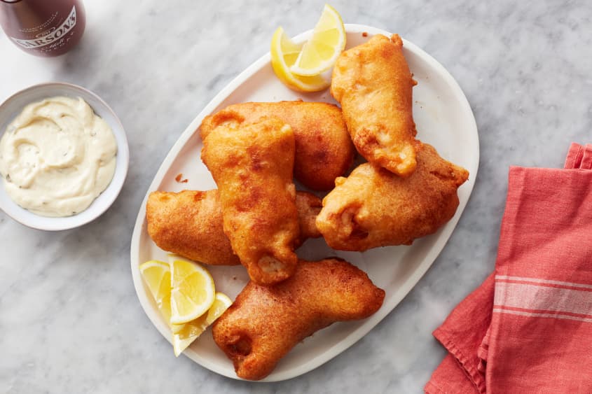 beer battered fish sits on a plate next to tartar sauce and lemon wedges