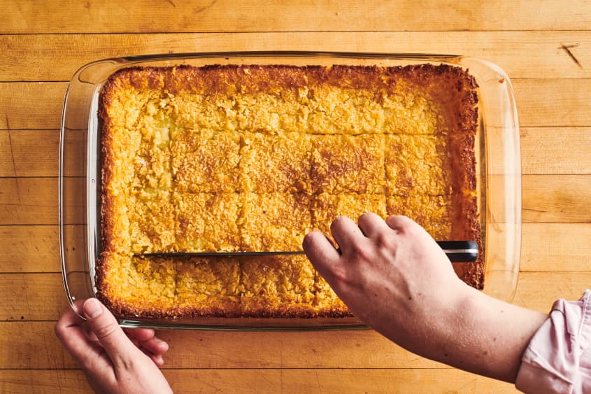 someone is slicing hawaiian butter mochi in a baking sheet