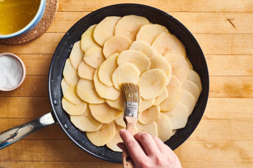 someone is brushing butter onto pommes anna