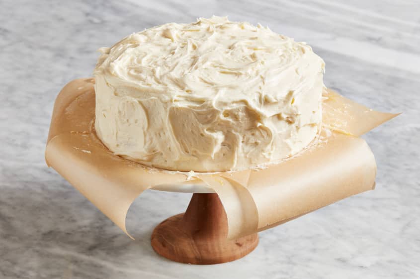 lemon coconut cake sits on parchment on a cake stand