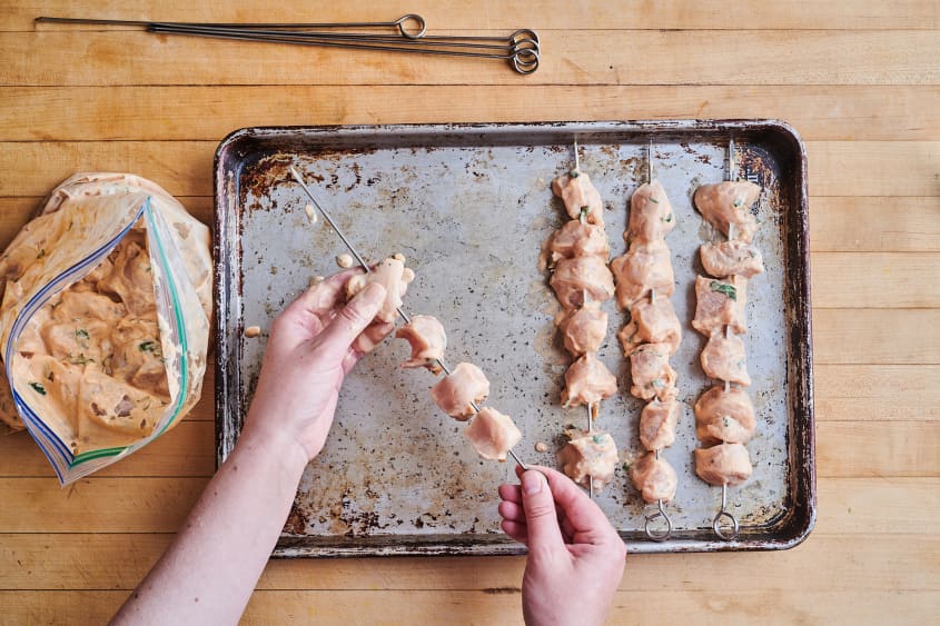 someone is making raw chicken kebabs on a sheet pan
