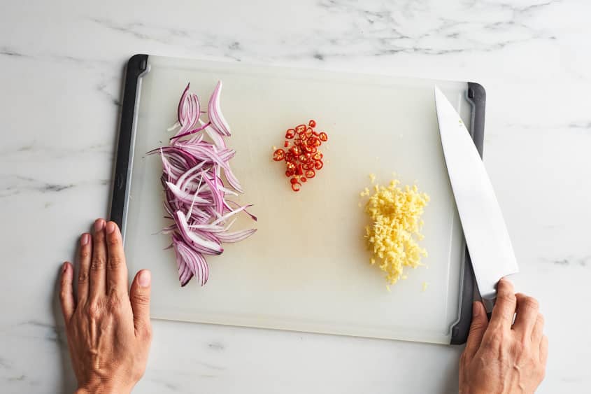 someone is slicing shallots peppers and ginger on a cutting board