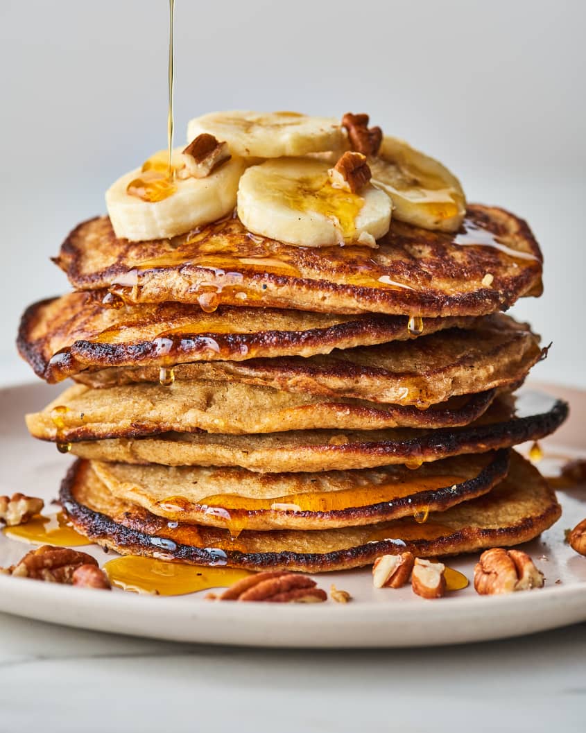 pancakes stacked with bananas on top being drizzled with syrup