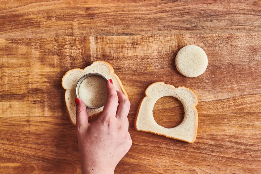someone cutting holes out of bread with a cookie cutter