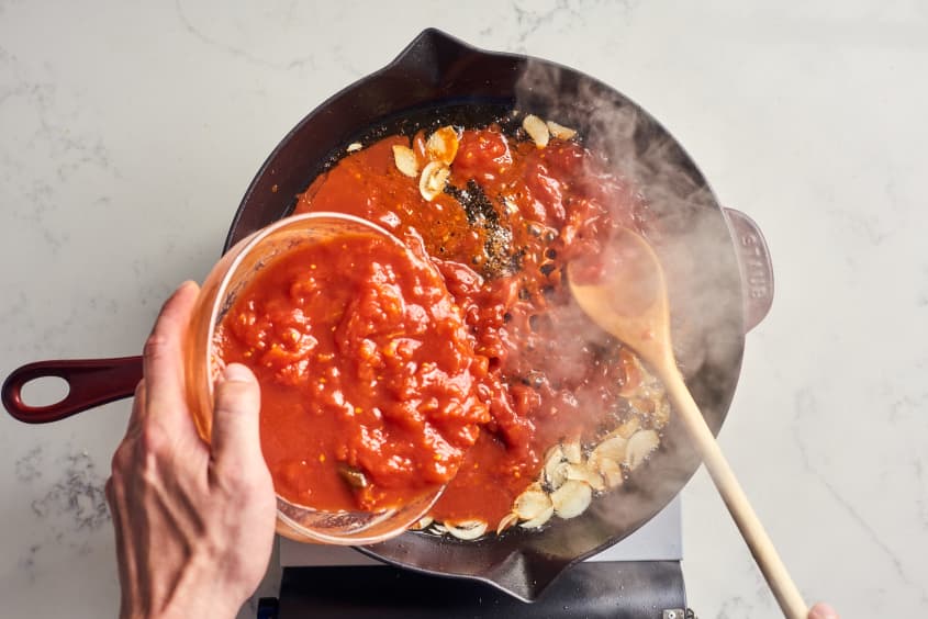someone pouring sauce over pasta in cast iron pan