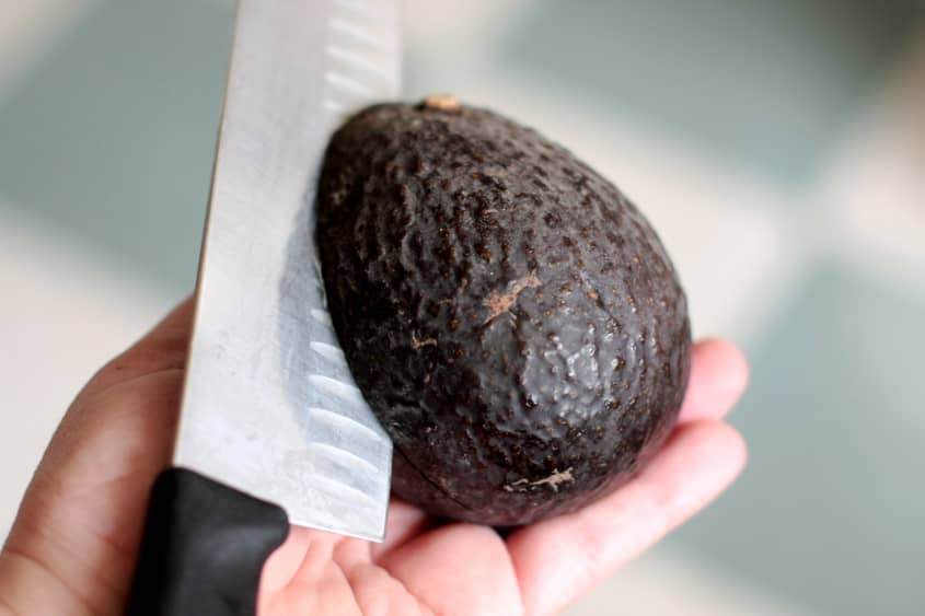 Hand holding an avocado with a knife slicing through the skin.
