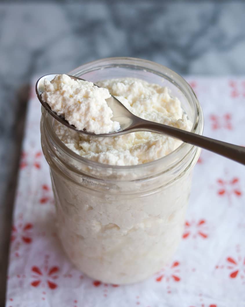 Open jar filled with homemade ricotta, a spoon perched on top