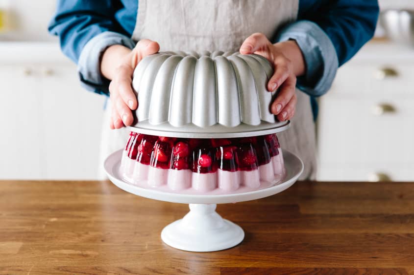 Someone removes the jelly mold to show the final product on a cake stand