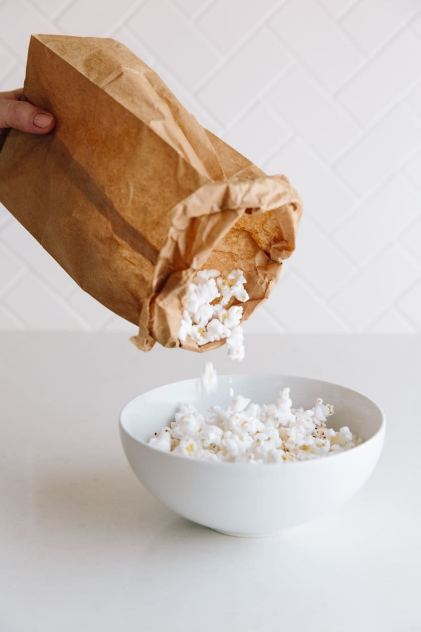 Someone transfers popcorn from a plain brown paper lunch bag into a bowl