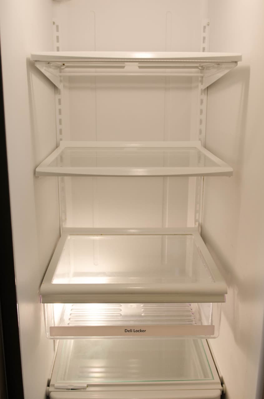 Empty refrigerator interior with glass shelves and a deli locker drawer.