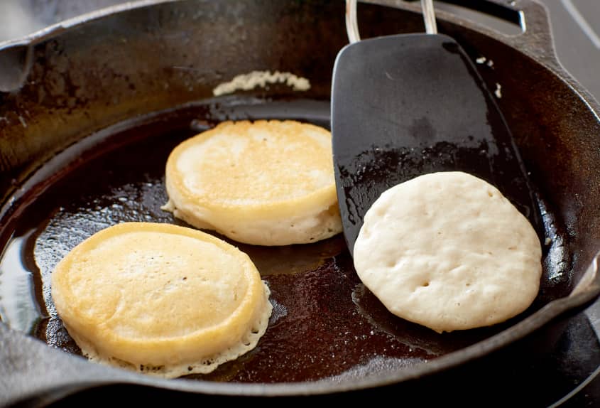 Pancakes cooking in a cast iron pan, a spatula flipping one