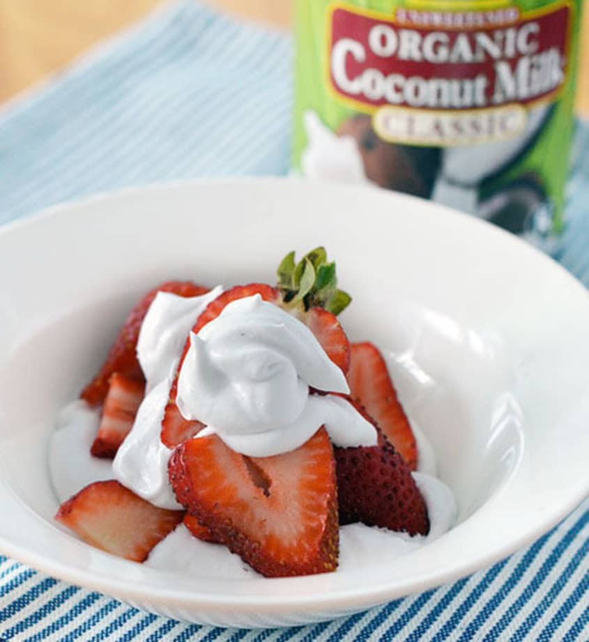 Fresh sliced strawberries with whipped cream, with a can of organic coconut milk in the background