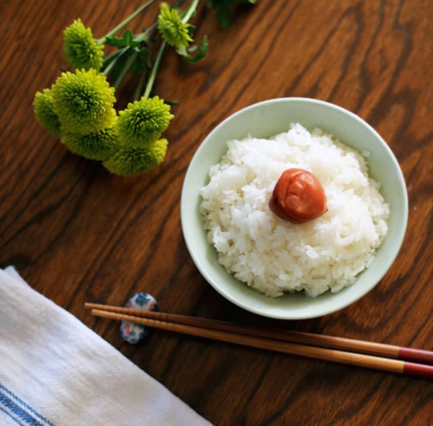 Japanese rice in a mint green-colored bowl, with chopsticks on the side