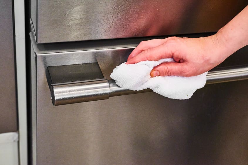 A hand wiping down the handle of a stainless steel appliance with a clean white cloth