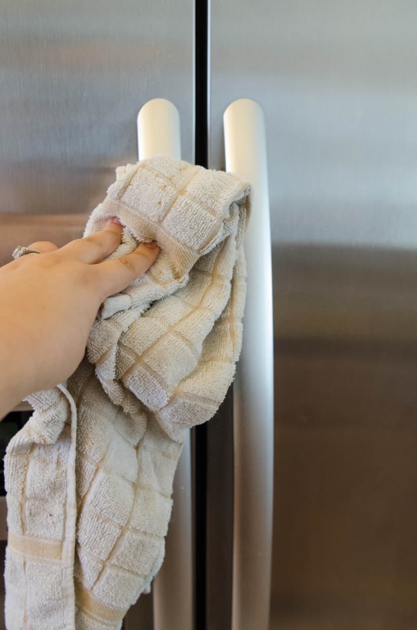 Hand cleaning stainless steel refrigerator handle with a beige cloth.