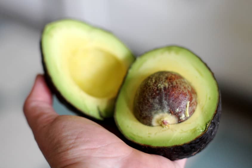 A hand holding a halved avocado with the pit visible.