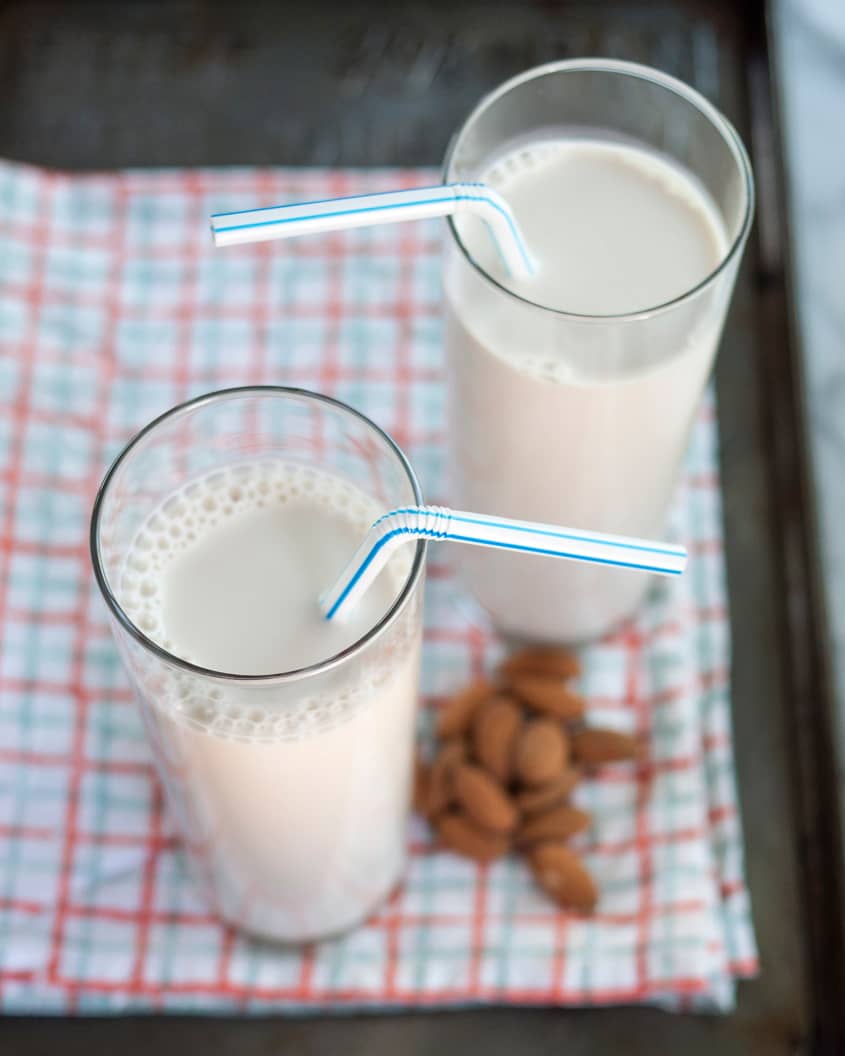 Overhead shot of two glasses filled with almond milk next to a handful of whole almonds