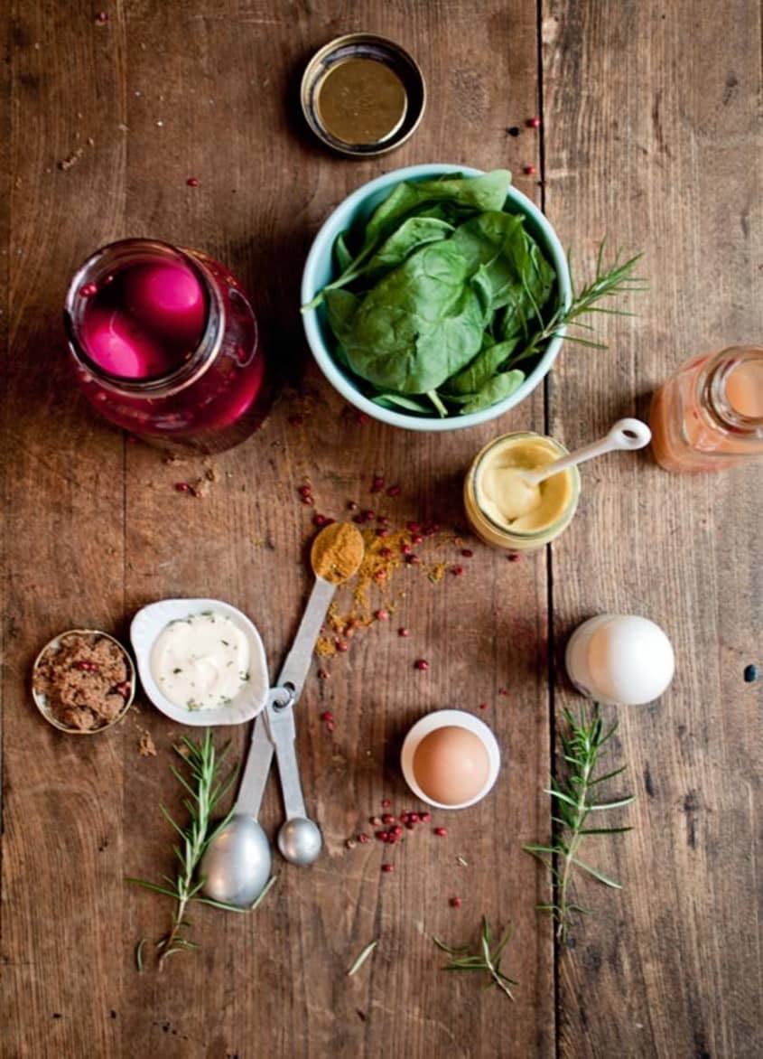 Ingredients for beet-pickled deviled eggs: jar of pickled beets, mustard, measuring spoons, mayonnaise, fresh rosemary, brown sugar, plus spinach leaves