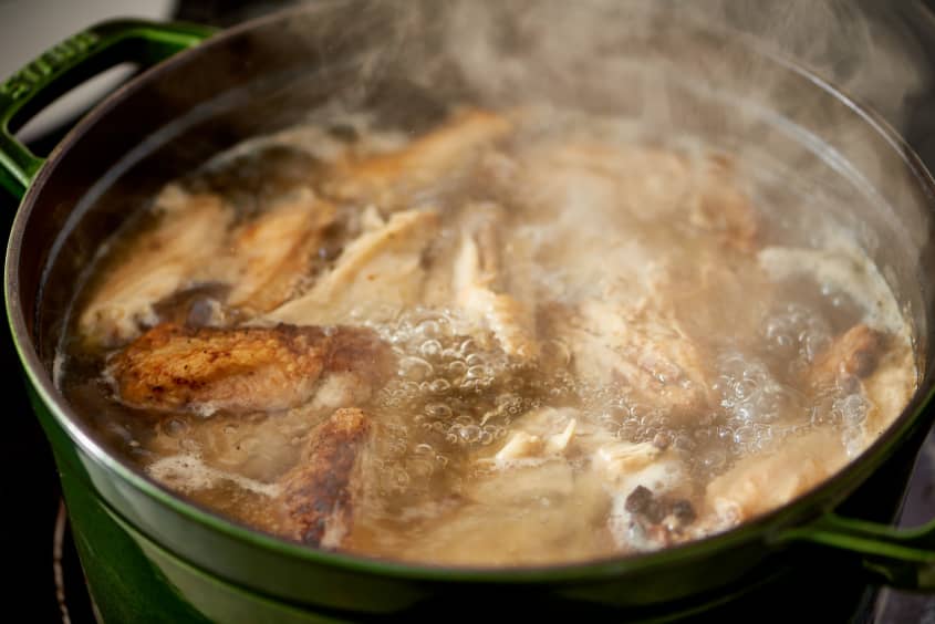 Bone-in chicken thighs and wings are cooked in  forest green-colored pot under low heat
