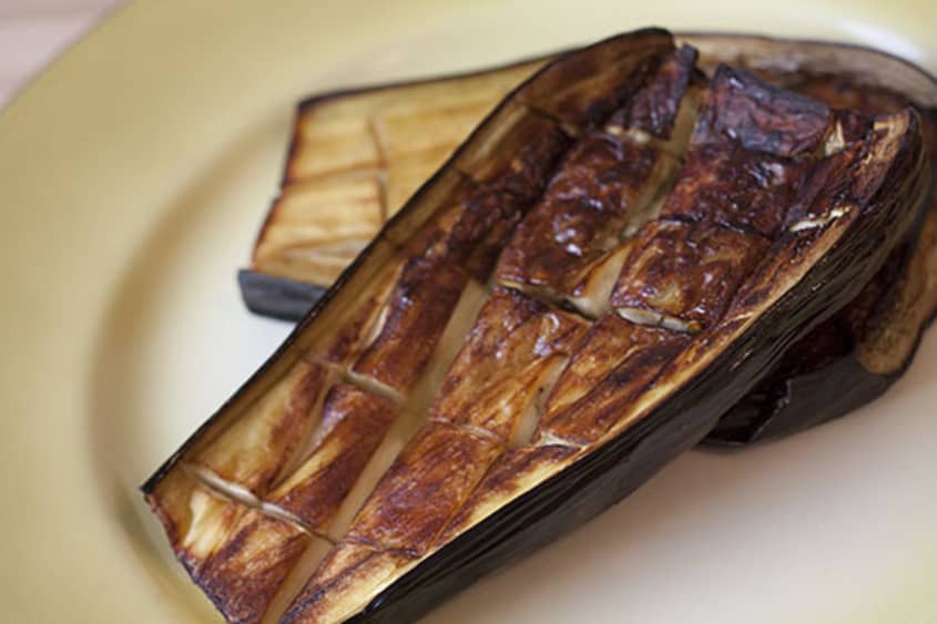 Roasted eggplant, cut diagonally in the middle, on a yellow plate