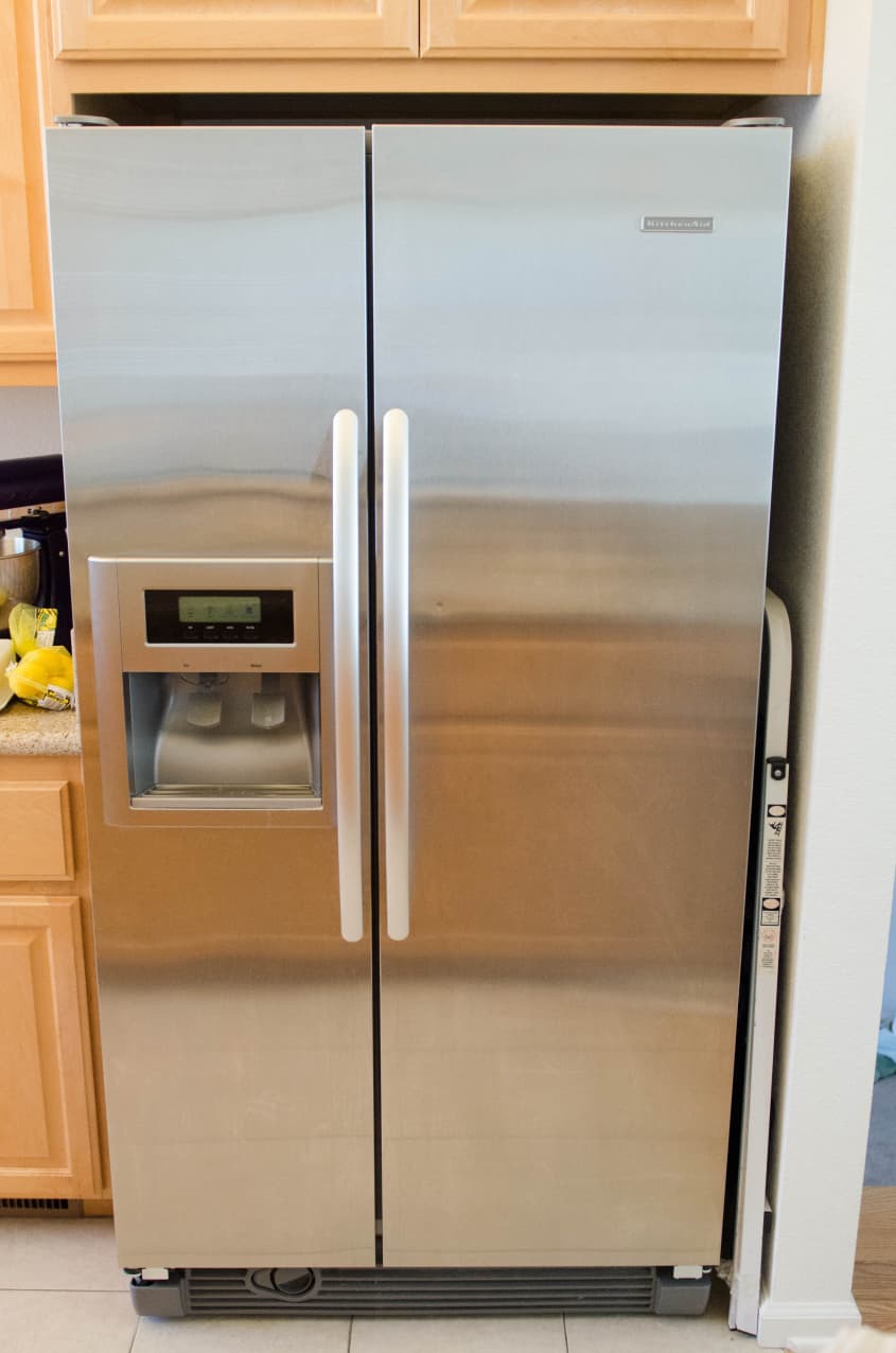 Stainless steel side-by-side refrigerator with ice and water dispenser, set between light wood cabinets.