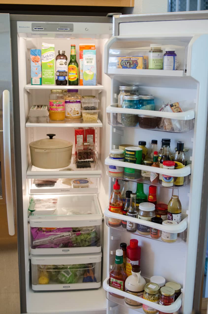 Open refrigerator with various condiments, sauces, and fresh produce.