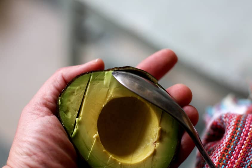 Hand holding a halved avocado with a spoon scooping out the flesh.