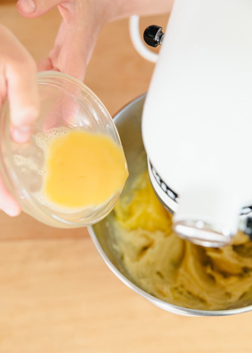 Someone adds egg yolks to the dough mixture in a stand mixer