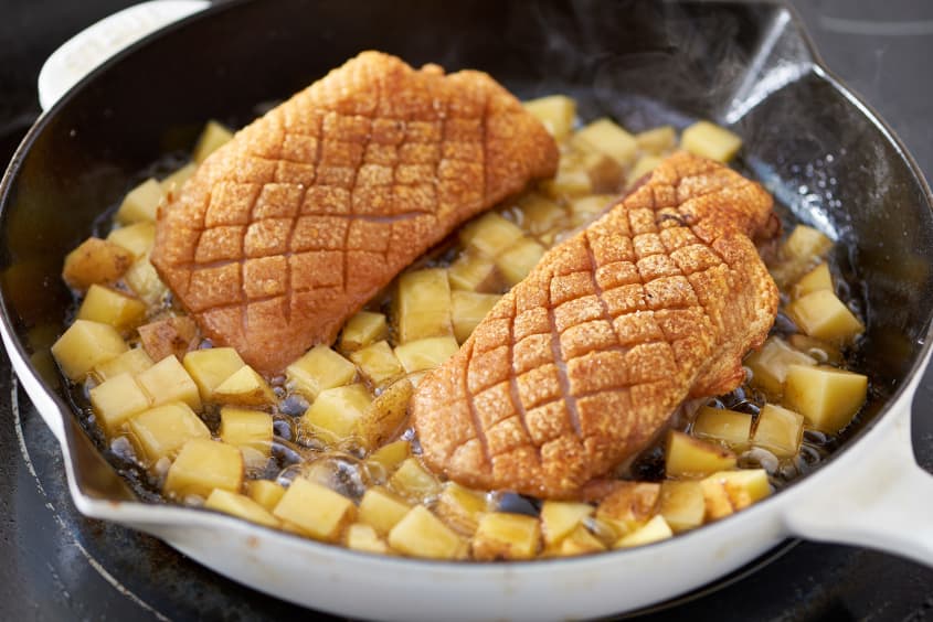 Cooking chopped potatoes and two duck breasts skin-side up on a cast iron pan