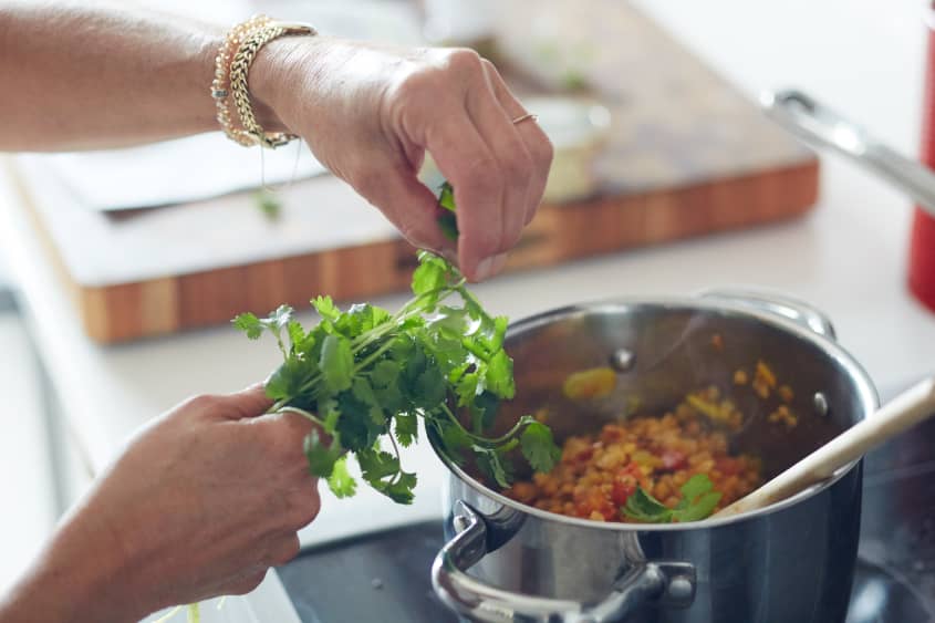 A person picks fresh cilantro leaves and putting it into a pot of dal