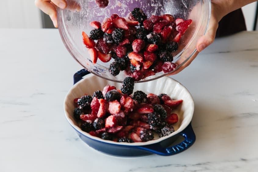 Mixed berries are transferred from a mixing bowl to a Staub cookware