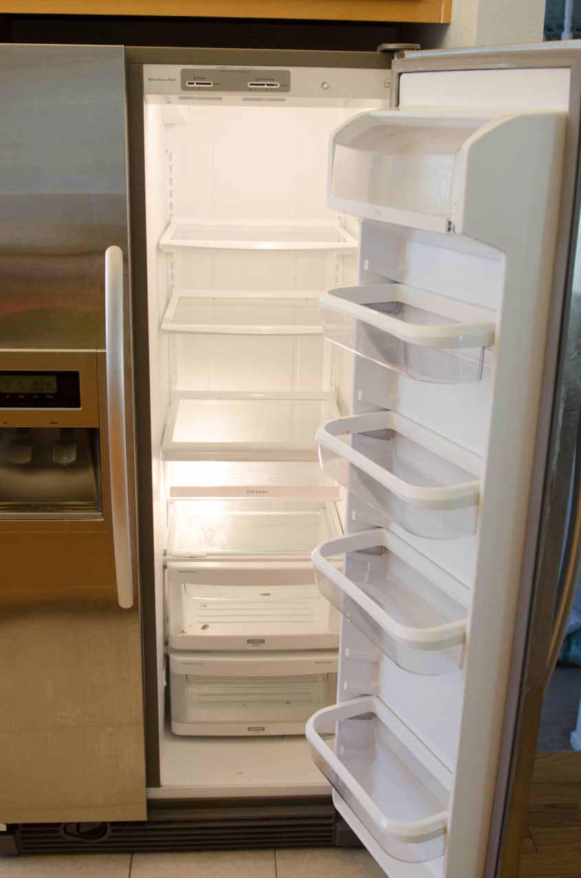 Open stainless steel refrigerator with empty shelves and door bins.